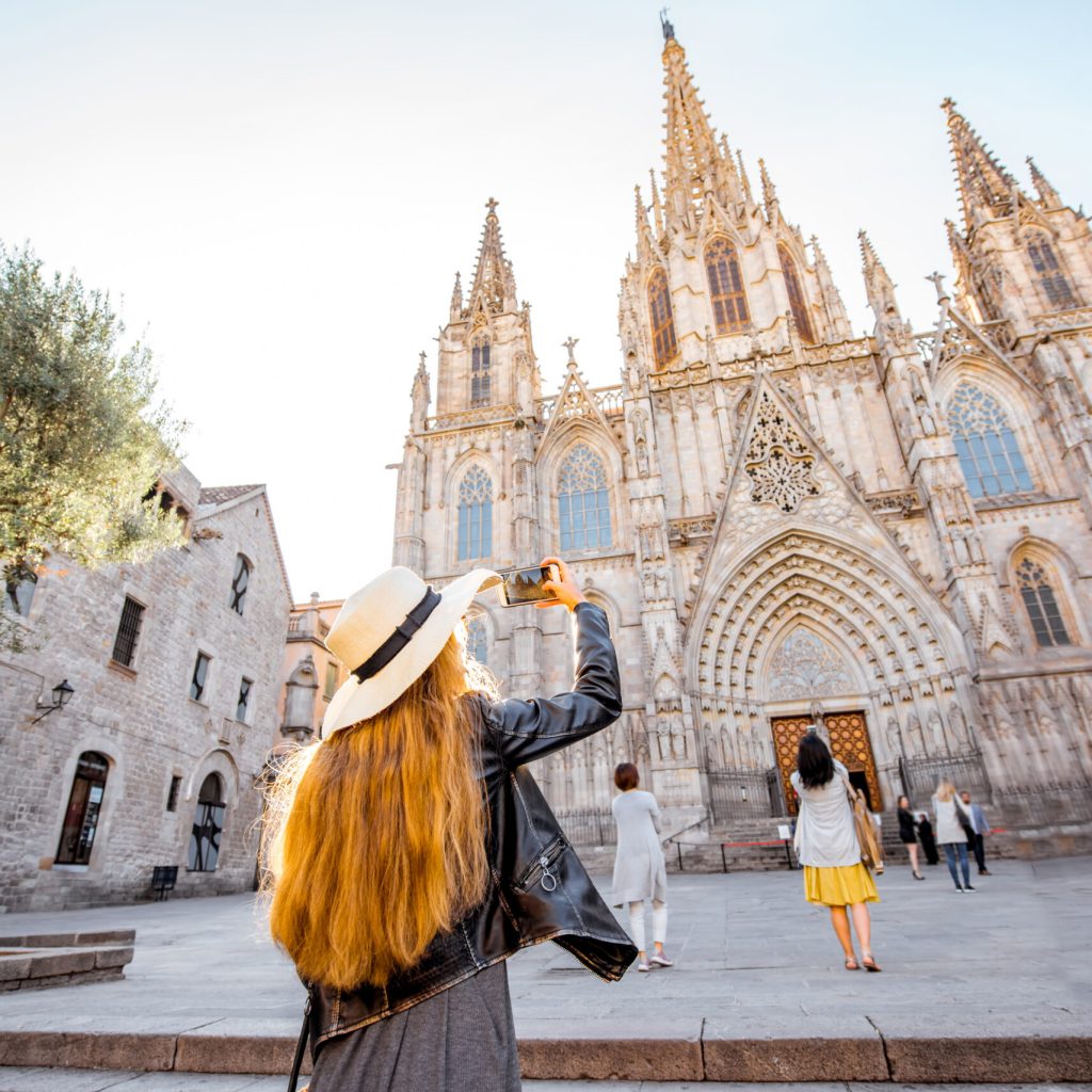 Young woman tourist photographing with phone famous saint Eulalia church during the morning light in Barcelona city